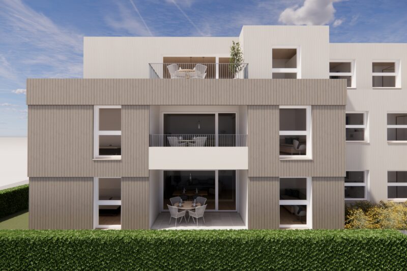 Moderne Fassade eines mehrstöckigen Wohngebäudes mit großen Fenstern und Balkonen, umgeben von einem gepflegten Heckenbereich unter blauem Himmel.