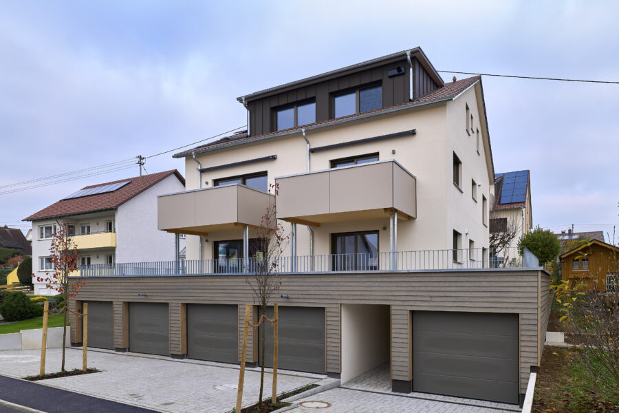 Moderne, dreistöckige Wohnhausarchitektur mit zwei hervorspringenden Balkonen und schmucklosen Garagen im Erdgeschoss, in einer ruhigen Wohngegend gelegen.