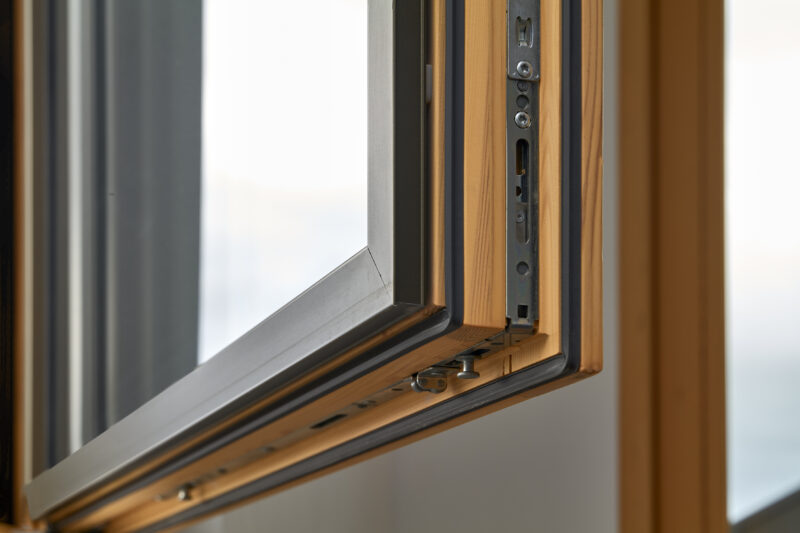 Detailansicht eines halb geöffneten, modernen Holzfensters mit sichtbaren Beschlägen.