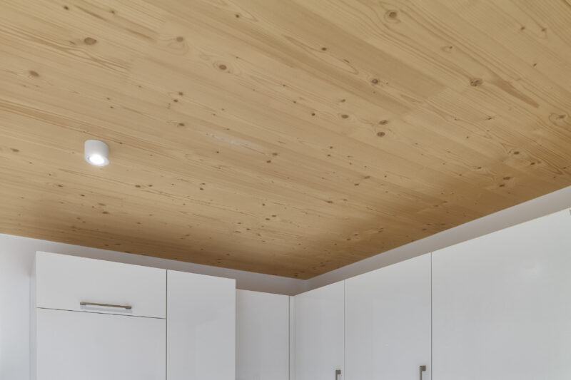 Holzvertäfelte Decke mit eingebauter LED-Leuchte über weißen Küchenschränken.
