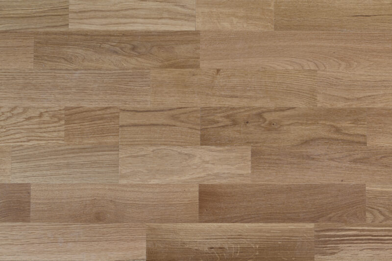 Beige- und braunfarbene Holzparkettoberfläche mit sichtbarer Maserung und natürlichem Glanz.
